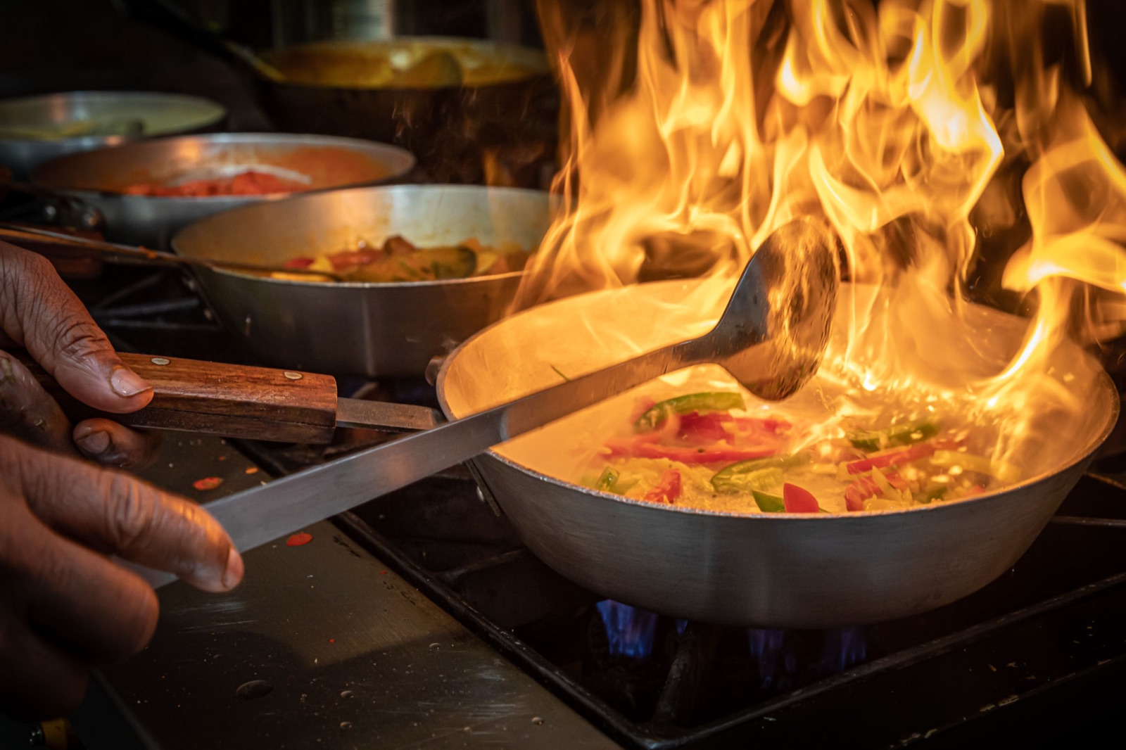 A chef tossing a flaming pan over the burners in the Bo&rsquo;ness Spice kitchen